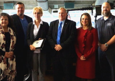 A picture of people together. They seem happy, formal, and diverse. They are all looking at the camera smiling, and a woman is carrying a diploma.