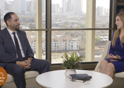 A corporate picture of a man and a woman talking. They are sitting in separate chairs and there is a little round table with a plant on the top of it. The man is wearing a suit and the woman is wearing a blue dress, they seem professional and friendly. There is a logo in the bottom right corner of the image that says: “Workforce Solutions”.