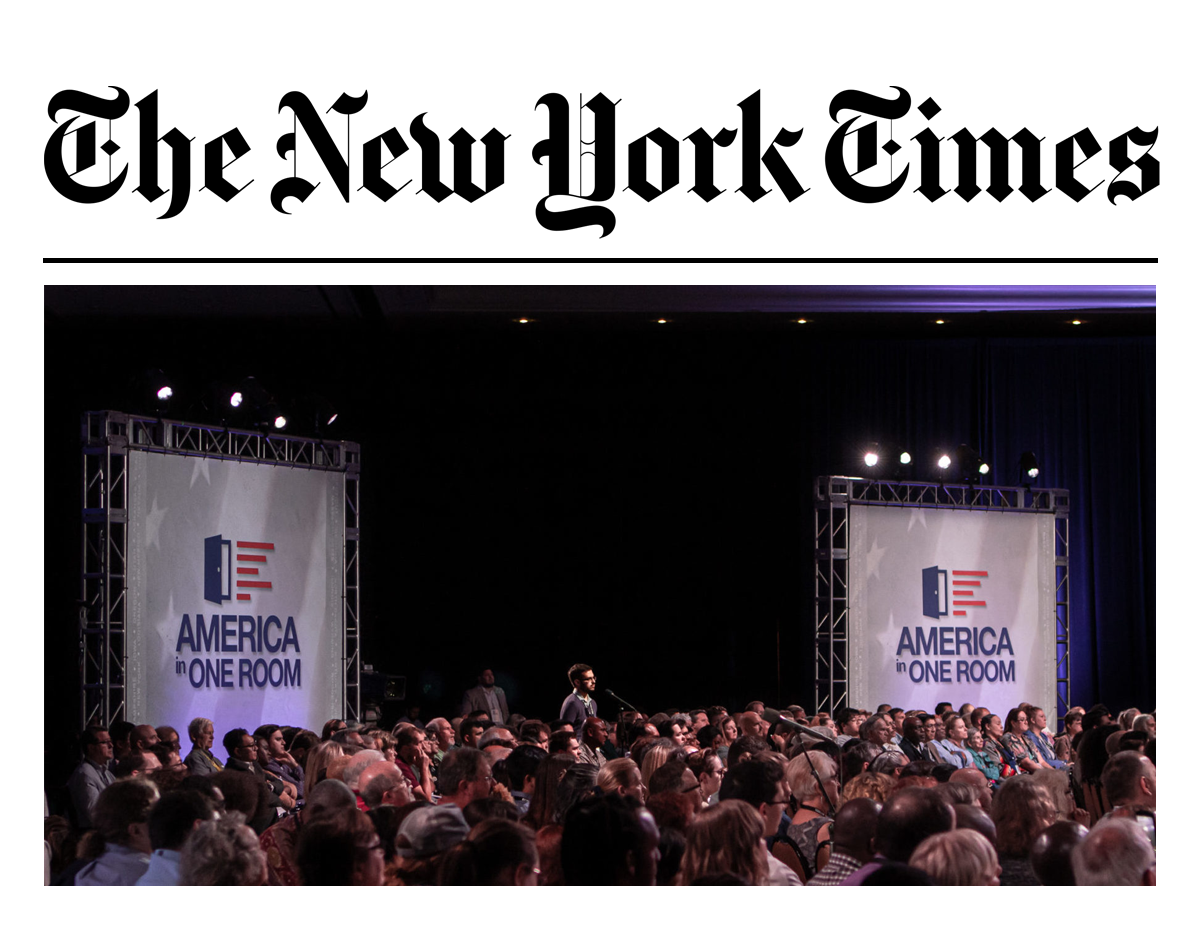 A picture of a big conference, with many people attending it. Al people seem sitting and watching something in front of the. At the back of the conference room there is the logo of “America in one room”.